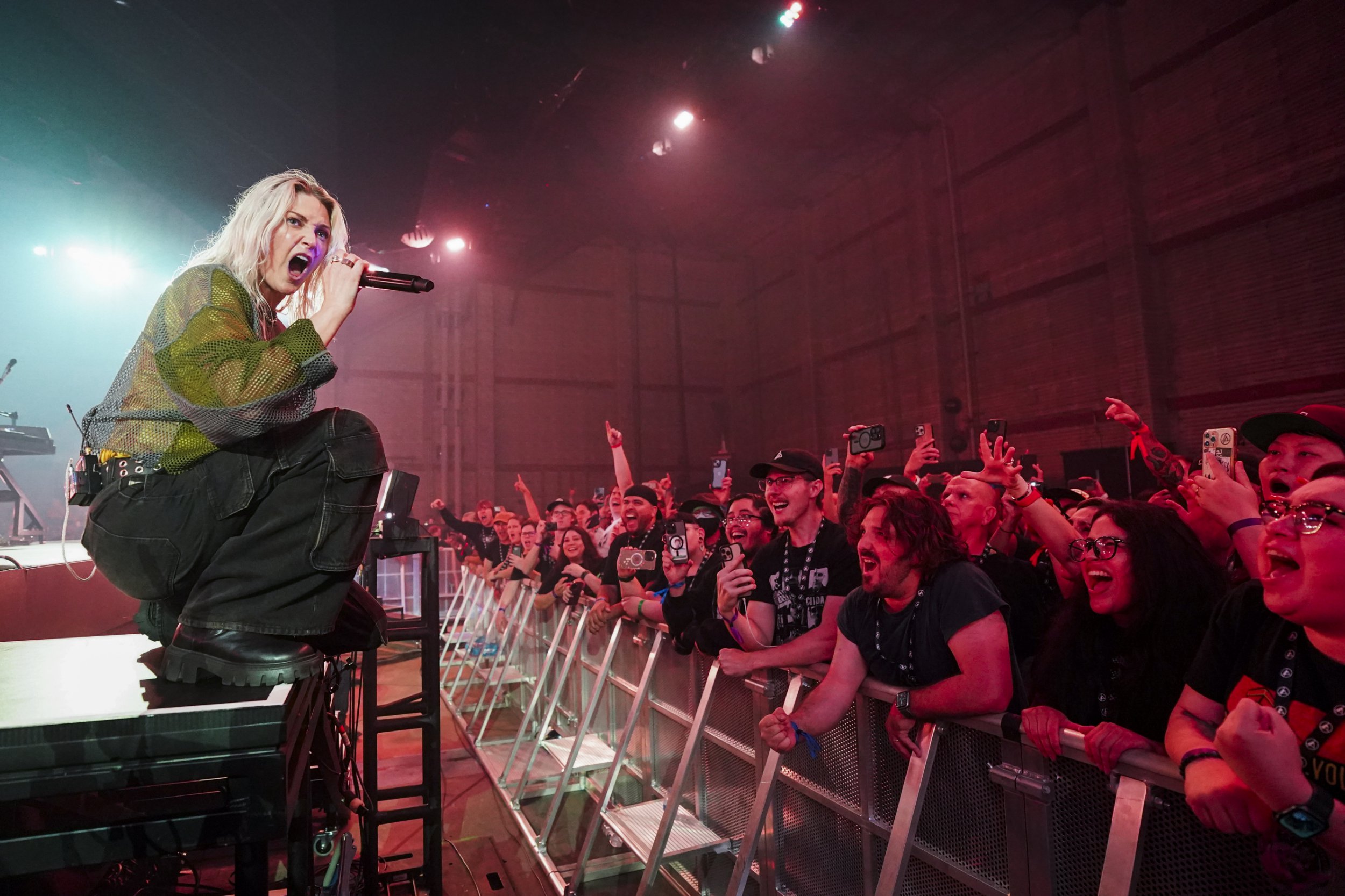 Emily Armstrong of linkin Park crouches down as she performs on stage to a shouting crowd